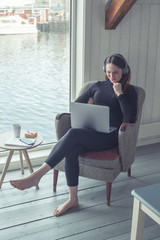 Young woman is siting in a modern scandinavian apartment. She is fulfilling her free time at home with digital entertainment. She is taking a break from exhausting  home office or distance education. 