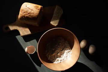 ingredients for bread and bread itself on a dark background.