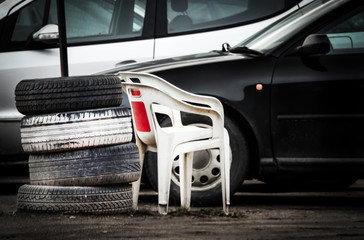 Fototapeta premium White plastic chairs standing near tires and cars