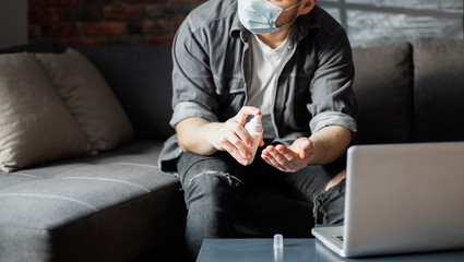 Coronavirus. Man working from home wearing protective mask and cleaning hands with sanitizer at quarantine