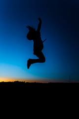 Silhouette of a girl in a jump on a background of sunset and a dark blue sky