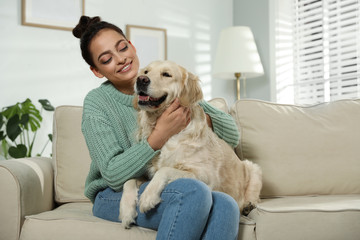 Young woman and her Golden Retriever on sofa at home. Adorable pet