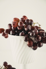 Closeup of dark red grapes in an old white bowl on a white table