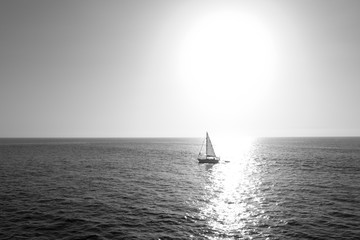 white sailboat far into the sea against the sun, black and white photo