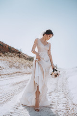 Fototapeta na wymiar Beautiful brunette bride with stylish make-up in white dress in spring nature