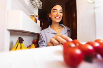 Young woman taking fresh tomato from refrigerator