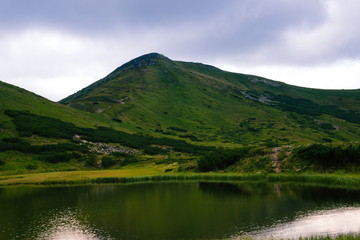 Carpathians mountains in the middle of summer. Nesamovite lake on the top of hill. Green hill. Ukrainian popular tourism place with calm water and shrubs. Mountain hiking. Walking on the top. View.