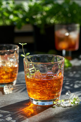 orange summer cocktail with ice on dark background. Shadows of glasses, hard sun light.