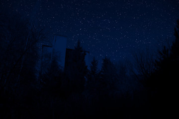 Mountain night landscape of building at forest at night with moon or vintage country house at night with clouds and stars. Cold autumn night