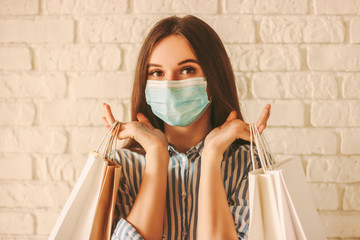 Beautiful girl shopper in medical face mask holding shopping bags in hands. Young happy woman...