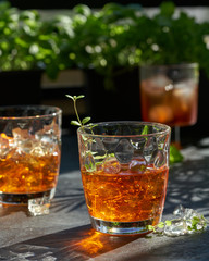 orange summer cocktail with ice on dark background. Shadows of glasses, hard sun light.