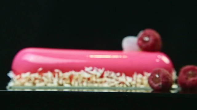 focus out from pink glazed eclair decorated with coconut shavings and raspberries