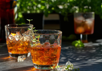 orange summer cocktail with ice on dark background. Shadows of glasses, hard sun light.