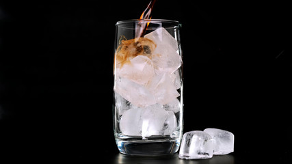 Pouring Cola with ice cubes in glass on black background. Close up.