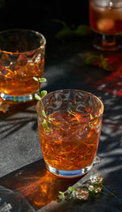 orange summer cocktail with ice on dark background. Shadows of glasses, hard sun light.