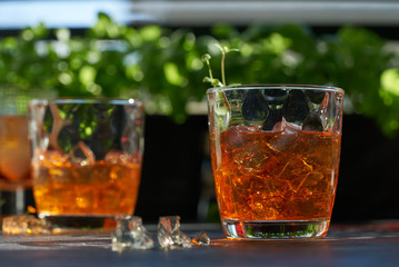 orange summer cocktail with ice on dark background. Shadows of glasses, hard sun light.