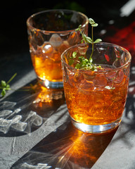 orange summer cocktail with ice on dark background. Shadows of glasses, hard sun light.