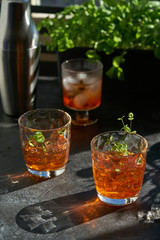orange summer cocktail with ice on dark background. Shadows of glasses, hard sun light.