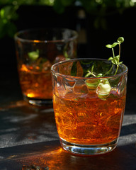 orange summer cocktail with ice on dark background. Shadows of glasses, hard sun light.