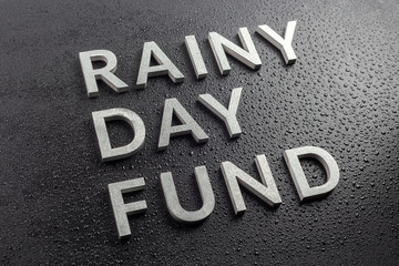 the words rainy day fund laid with silver metal letters on black background, covered with water...