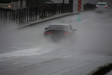 cars drive in heavy rain along the road, spraying fountains of water from puddles in all directions