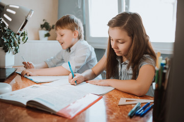 The girl and boy writing them homework in the copybook at home during CoVid-19 quarantine, distance learning online with a laptop, a child doing homework for school. Children stayed at home.