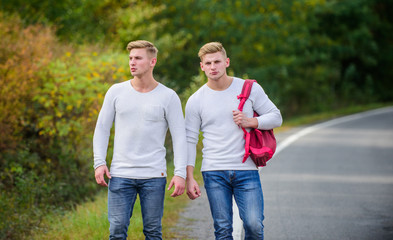 means of travel. twins walking along road. two brothers go adventure. friendship. men hitch hiking. man casual style travel with backpack. traveler hitchhiking on highway. on the way home. future