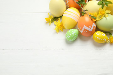 Colorful Easter eggs and flowers on white wooden table, flat lay. Space for text