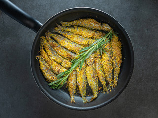 over head view to fried sea fish with herbs in black bowl on dark background