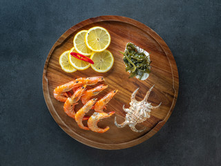 round wooden plate with srimps and lemon slices on black background