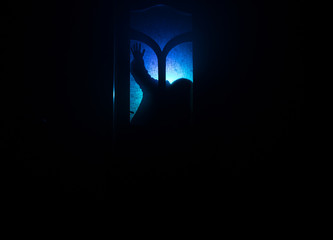 Silhouette of an unknown shadow figure on a door through a closed glass door. The silhouette of a human in front of a window at night. Scary scene halloween concept of blurred silhouette of maniac.