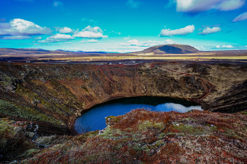 The Kerid Volcanic crater and the deep water lake at the bottom of the volcano surrounded by the volcanic red rocks and moss and lichen