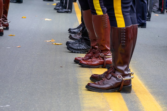 Police officers standing on a yellow line in the middle of a paved road. The officers have a yellow stripe on their pants and brown leather boots. There are multiple rows of men on parade.