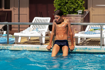 A sad lonely boy sits on board a swimming pool and is bored. The concept of loneliness and depression.