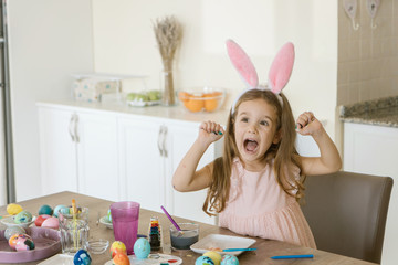 sweet cute girl in a bunny ears so happy while painting eggs for easter day.