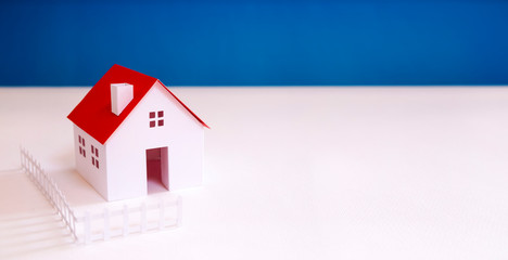 white paper miniature house with red roof on blue color background