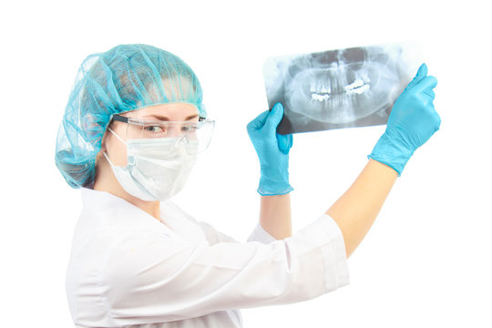 young female doctor in transparent safety glasses wearing a cap and white coat and blue gloves holds a panoramic x-ray picture of teeth in his hands on a white background in studio