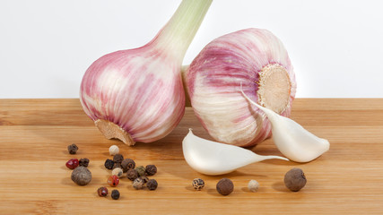 Close up of garlic bulbs and peppercorns on wooden cutting board