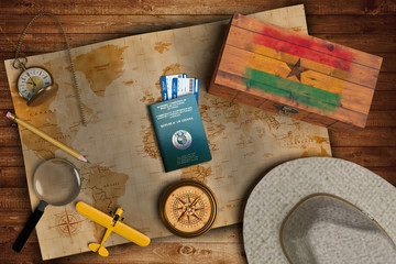 Top view of traveling gadgets, vintage map, magnify glass, hat and airplane model on the wood table background. On center, official passport of Ghana and your flag. - obrazy, fototapety, plakaty