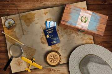 Top view of traveling gadgets, vintage map, magnify glass, hat and airplane model on the wood table background. On center, official passport of Guatemala and your flag.