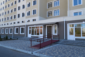 Wheelchair access ramp for entrance of residential multistory building, city street and tiles sidewalk