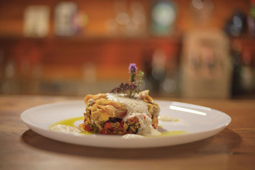 Medallion with yellow sauce on a white plate with a flower on top close-up on a wooden table