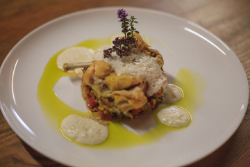 Medallion with yellow sauce on a white plate with a flower on top close-up on a wooden table