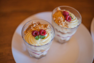two desserts in glass glasses white cream with two raspberries and leaves top view close-up