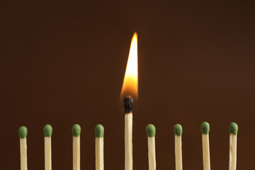 Burning match among unlit ones on brown background, closeup