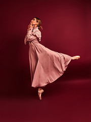 Fototapeta premium Ballet dancer or classic ballerina dancing isolated on red background. The dance, grace, artist, contemporary, movement, action and motion concept