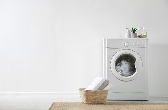 Modern washing machine and laundry basket near white wall indoors, space for text. Bathroom interior