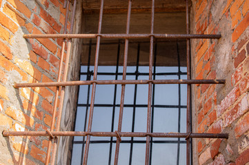A prison window in a brick wall behind a metal grating