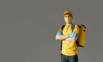 Safe food delivery. Courier in yellow uniform, protective mask and gloves delivers takeaway food during coronovirus quarantine. Copy space for text
