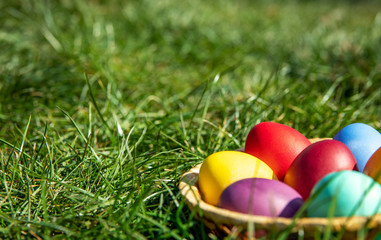 Multi-colored Easter eggs in a basket on the grass, the background is blurred, shallow depth of field, selective focus. Easter holiday concept